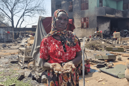 Eine zweifach vertriebene Mutter zeigt Kugeln vor einem niedergebrannten Gebäude.