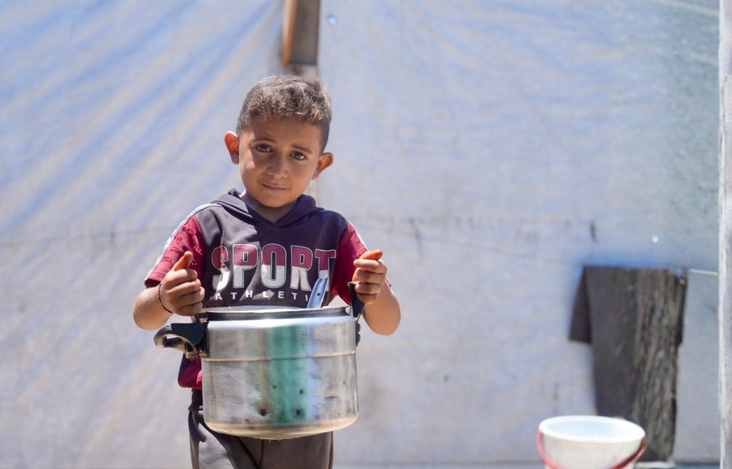 Kind in Gaza trägt ein Topf mit Wasser zum Zelt